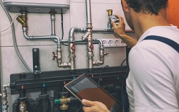 technician checking the heating system in the boiler room with tablet in hand