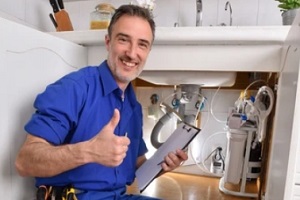 technician checking water installation under the sink of a home kitchen with notepad